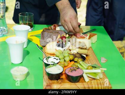 Auswahl an Vorspeisen auf dem grünen Tisch. Hand des Mannes, der ein Stück Käse mit Zahnstocher unter salzigen, süßen Snacks serviert Stockfoto