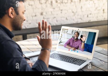 Zwei männliche Kollegen begrüßen sich während eines Videotreffens. Multirassische Geschäftspartner beteiligten sich an einer virtuellen Konferenz. Zurück Ansicht männlicher Schüler nimmt einen Online-Sprachkurs von afrikanischem Lehrer Stockfoto