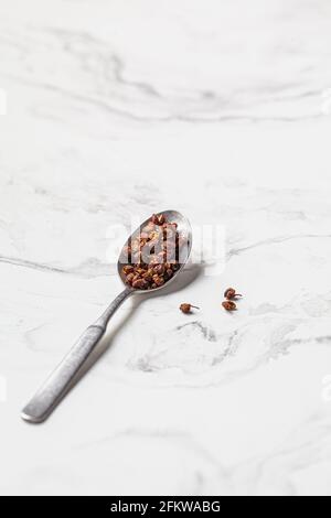 Sichuan-Pfefferkorn in einem Löffel auf weißem Marmorboden. Stockfoto
