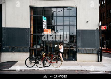 New York City, USA - 20. Juni 2018: Menschen, die auf der Straße in Dumbo (Brooklyn) vor dem Ladenlokal mit geparkten Fahrrädern laufen. Stockfoto