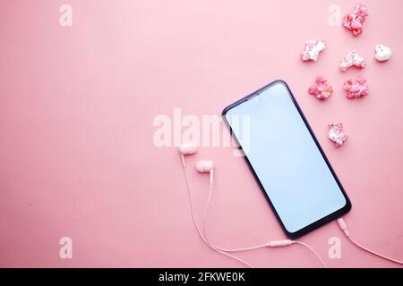Draufsicht auf Smartphone, Ohrhörer und Popcorn in Pink Stockfoto