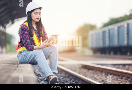 Porträt einer schönen Frau, die mit einem Tablet mit einem Hardhut vor der Zuggarage unterwegs war. Stockfoto