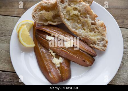 kipper-Schnitzel aus geräuchertem Craster auf einem Holzhintergrund. Kipper sind geräucherte Heringe und sind reich an Fischölen. Serviert mit warmem Brot, Butter Stockfoto