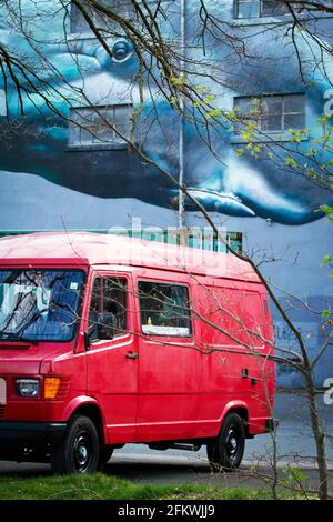 Red Van, geparkt vor EINEM Gebäude mit EINEM riesigen Wal als Graffiti an EINER Hausfassade Stockfoto