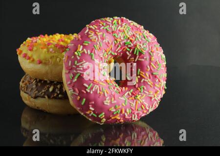 Donuts mit Vereisung liegen Stops und rosafarbene, helle Stative auf schwarzem Hintergrund mit Platz für Text. Stockfoto