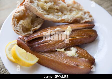 kipper-Schnitzel aus geräuchertem Craster auf einem Holzhintergrund. Kipper sind geräucherte Heringe und sind reich an Fischölen. Serviert mit warmem Brot, Butter Stockfoto