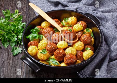 Fleischbällchen und Spaghettibällchen auf einer schwarzen Backform gebacken - italienische Küche, serviert auf dunklem Holzboden mit frischer Petersilie und Holzlöffel, Stockfoto