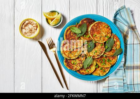 Kichererbsen Spinat Pfannkuchen auf einem blauen Teller auf einem weißen Holztisch mit Hummus in einer kleinen Schüssel, flach liegend, freier Platz Stockfoto