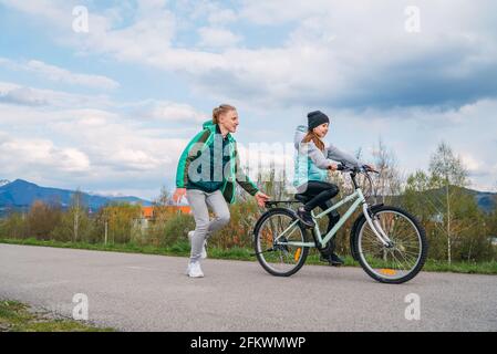 Lächelnde Kinder auf einem Fahrrad Asphalt Weg. Bruder hilft der Schwester und lehrt erste Schritte im Reiten. Happy Kindheitskonzept Bild. Stockfoto