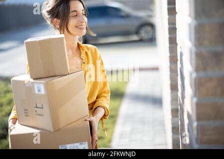 Eine junge glückliche Frau trägt ein Päckchen mit online gekauften Waren nach Hause und klopft an die Tür. Konzept von Online-Shopping und -Lieferung. Stockfoto