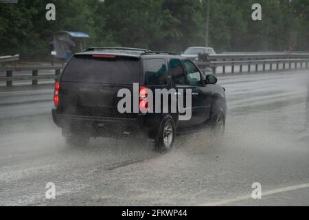 Ein schwarzer SUV fährt im Regen auf der Autobahn. Das Auto fährt schnell auf nasser Straße. Das Auto fährt durch eine Pfütze. Das Auto fährt vorwärts. It“ Stockfoto