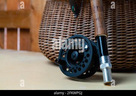 Nahaufnahme der Fliegenfischerei mit Rolle neben geflochtenem Korb. Fliegenfischen Ausrüstung Stillleben. Niemand Stockfoto