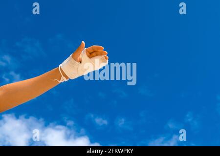 Gebrochene Hand in weißem Cast auf blauem Hintergrund mit Platz für Text. Trauma mit dem Finger. Stockfoto