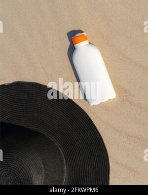 Sonnencreme neben einem schwarzen Hut auf dem Sand an einem sonnigen Tag am Strand. Kin Schutz Kosmetik zum Sonnenbaden. Niemand Stockfoto