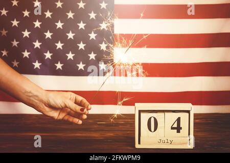 Retro getönter kurzer Schuss, Frau mit brennendem Funkler, bengalisches Licht auf amerikanischem Flaggenhintergrund. 4. Juli, USA Unabhängigkeitstag Datum auf Holz c Stockfoto