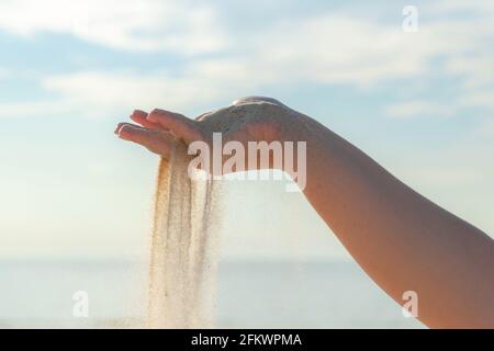 Nahaufnahme von Sand, der an einem sonnigen Sommertag aus der Hand auf den Strand fließt. Spielen mit Sand im Urlaub. Stockfoto