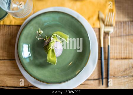 Happy Easter Konzept. Wunderschöne Frühlingsgedecke, grüner Teller mit Ei und Ast von Apfelblüten. Urlaub mit Tisch. Stockfoto