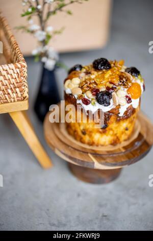 Köstlicher süßer Oster-Cupcake, verziert mit getrockneten Früchten und Nüssen auf hölzernen Kuchenständern und Frühlingszweig mit weißen Blumen in Vase. Stockfoto