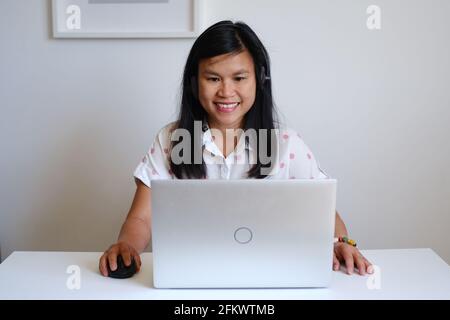 Filipino filipina Asiatische Lehrerin, die vor einem weißen Schreibtisch und silbernem Computer sitzt und online eine Lektion im Internet unterrichtet Stockfoto