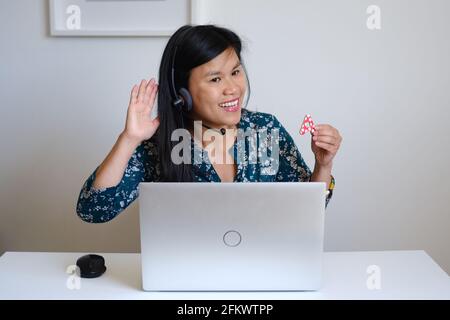 Filipino filipina Asiatische Lehrerin, die vor einem weißen Schreibtisch und silbernem Computer sitzt und online eine Lektion im Internet unterrichtet Stockfoto