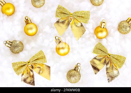 Leuchtend goldene und gelbe Weihnachtsdekorationen (Bänder, Kugeln, Ornamente) lagen flach auf weißem künstlichen Schnee Hintergrund. Weihnachten und Neujahr trad Stockfoto
