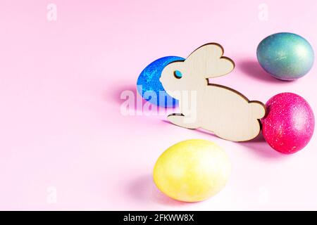 Lustiger Osterhase aus Holz mit bunten Eiern als Zeichen eines Urlaubs mit Kopierplatz auf hellrosa Hintergrund. Stockfoto