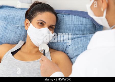Patientin in Maske, die eine Ärztin mit kranken Gesichtes anschaut. Stockfoto