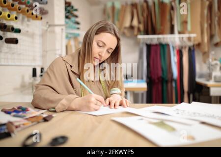 In ihrer Werkstatt arbeitet eine Modedesignerin. Stilvolle Frau im Prozess der Schaffung neuer Kleidung Kollektion. Stockfoto