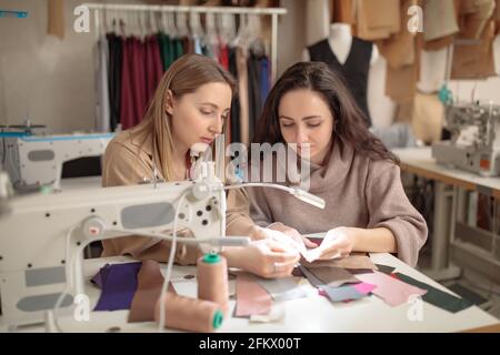 Zwei Modedesignerinnen schauten sich Muster von Skizzen an In einer Nähwerkstatt Stockfoto