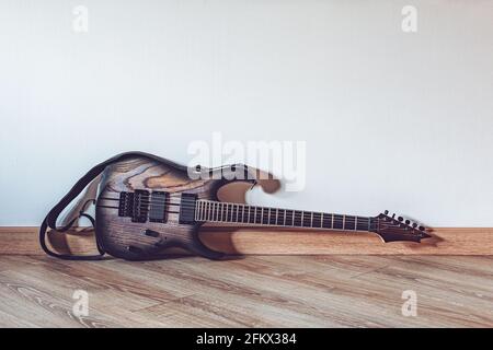 Elektrische Holzgitarre, die vor Weiß auf dem Boden liegt Wand mit Kopierbereich Stockfoto