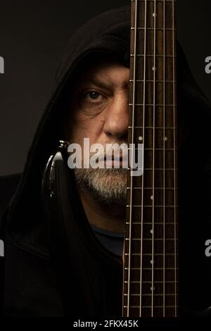 Ein Gesicht eines Mannes in einem Hoodie hinter einer Bassgitarre Stockfoto