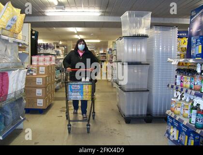 Weibliche Käuferin, die mit einem Gesicht den Einkaufswagen im Supermarkt schiebt Maske aufgrund einer Coronavirus-Pandemie Stockfoto