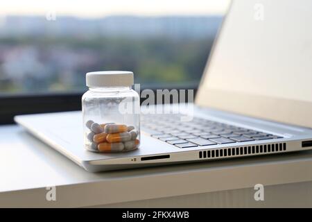 Pillen auf Laptop-Tastatur auf Fensterhintergrund, Kapseln in einer Flasche. Konzept der Einnahme von Medikamenten im Büro, Vitamine für Energie und Arbeit Stockfoto