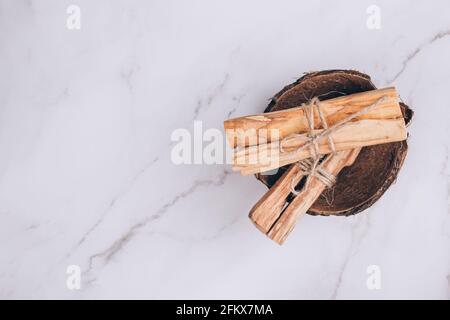 Palo Santo Baum klebt in der Kokosnussschale auf hellem Marmortischhintergrund - heiliger Weihrauchbaum aus Lateinamerika. Meditation, geistige Gesundheit und Stockfoto