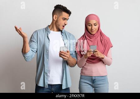 Datenschutzkonzept. Porträt eines schockierten arabischen Mannes, der das Smartphone der muslimischen Frau ansah Stockfoto