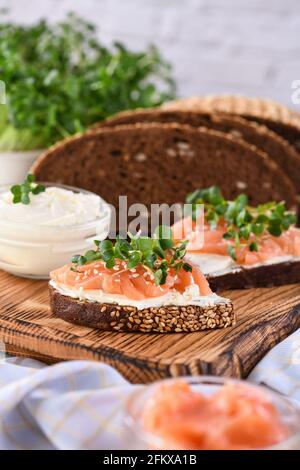 Offenes Sandwich mit Käsecreme auf einer Scheibe Roggenbrot mit Müsli, Scheiben mariniertem Lachs und Rettichsprossen. Stockfoto