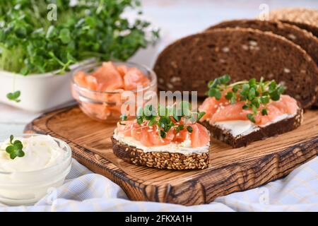 Offenes Sandwich mit Käsecreme auf einer Scheibe Roggenbrot mit Müsli, Scheiben mariniertem Lachs und Rettichsprossen. Stockfoto