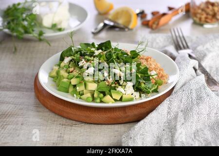 Glutenfreier grüner vegetarischer Salat aus mikrogrünen Sprossen Erbsen, Avocado, Quinoa, Spinat, gewürzten zerdrückten Mandeln mit Scheiben Feta-Käse Stockfoto
