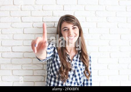 Schöne junge Frau berühren virtuellen Bildschirm Taste Konzept. Wunderschöne braune Augen tausendjährige Weibchen mit langen welligen dunklen Haaren mit perfekten Zähnen & Zeichen Stockfoto