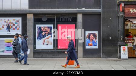 Ein edler Gentleman-Fußgänger geht an dem mit Plakaten bedeckten ehemaligen HMV-Laden in der Oxford Street, London, 4. Mai 2021, vorbei Stockfoto