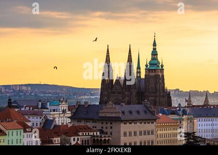 Prag, Tschechische Republik - Mai 3 2021: Blick auf die Prager Burg bei Sonnenaufgang. Orangefarbener und blauer Himmel im Hintergrund und zwei vorbeifliegende Vögel. Stockfoto