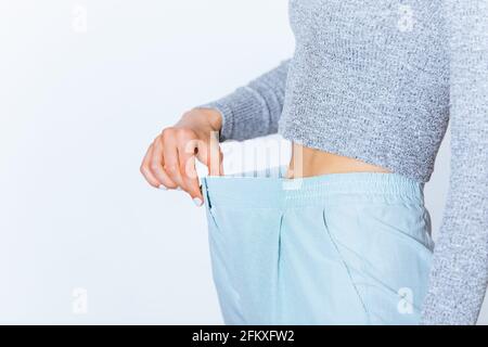 Gewichtsverlust junge Frau trägt große Hosen zeigt Fettabbau um ihre Taille, weißer Hintergrund. Stockfoto