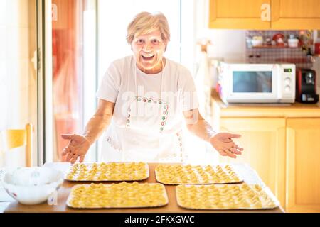 Glückliche Frau präsentiert handgemachte "Cappelletti" in der Hausküche - Regionales Food-Konzept mit hausgemachten italienischen Pasta-Zubereitung - warme helle Hintergrundbeleuchtung Stockfoto