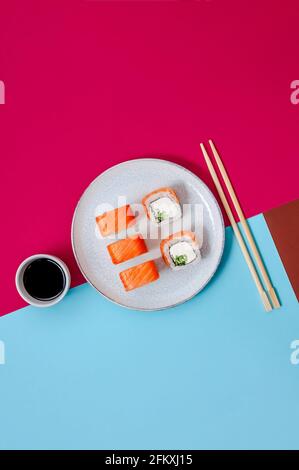 Philadelphia-Brötchen mit Lachsfisch, Gurke und Käse auf Teller mit Sojasauce auf buntem Hintergrund. Minimalkonzept Stockfoto