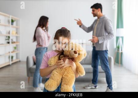 Familienkonflikte. Kleines Mädchen, das unter elterlichen Streitigkeiten leidet, ihren Teddybären kuschelt, sich einsam und deprimiert fühlt Stockfoto