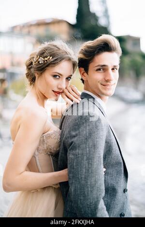 Lächelnde Braut umarmt sich von hinten, während sie auf der Promenade des Comer Sees steht. Stockfoto