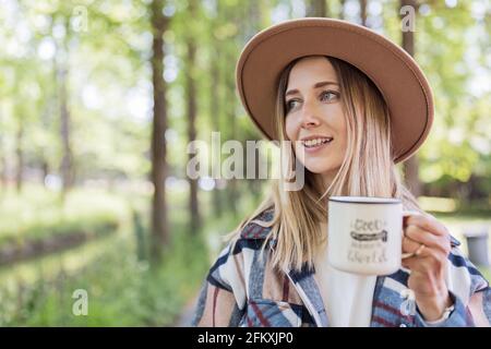 Junge stilvolle kaukasische Frau 30-35 Jahre alt in legerer Kleidung hemd und Cowboy Hut genießen das Leben am Morgen im Sommer Abenteuer im Camping Stockfoto