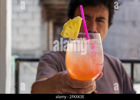 Mann hält einen Cocktail Tequila Sonnenaufgang mit Ananasscheibe für Konzept für Getränke im Frühling und Sommer Stockfoto