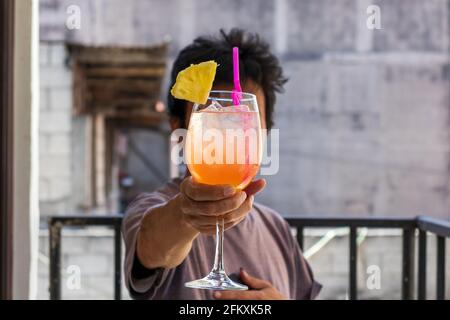 Mann hält einen Cocktail Tequila Sonnenaufgang mit Ananasscheibe für Konzept für Getränke im Frühling und Sommer Stockfoto