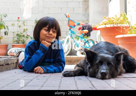 Junger hispanischer Junge, der mit einem alten schwarzen Hund spielt deutscher Schäferhund Stockfoto